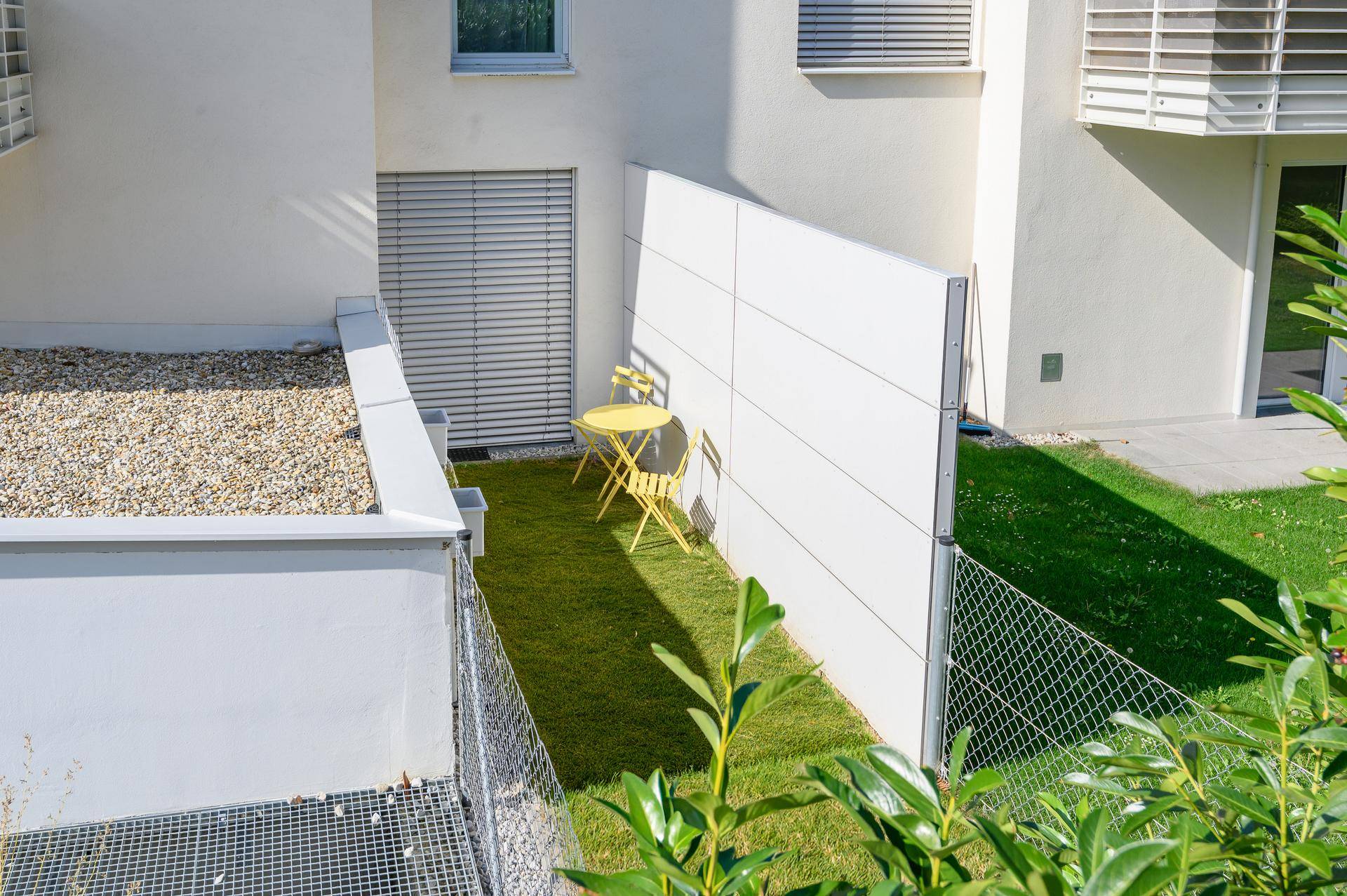 Kleiner privater Gartenbereich mit Rasenfläche und gelben Gartenmöbeln.