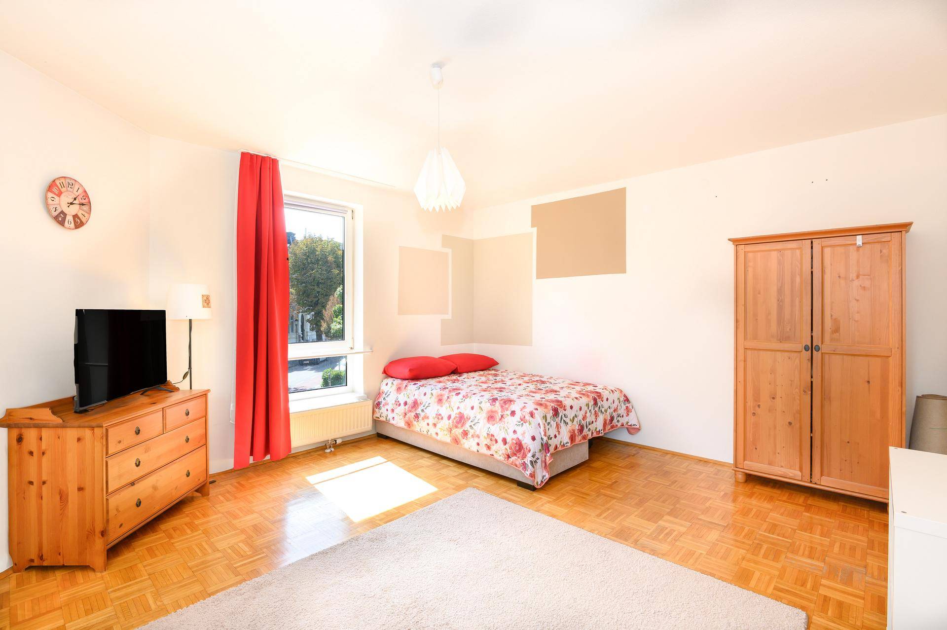 Geräumiges Schlafzimmer mit Holzboden, Kleiderschrank und Blick ins Grüne.