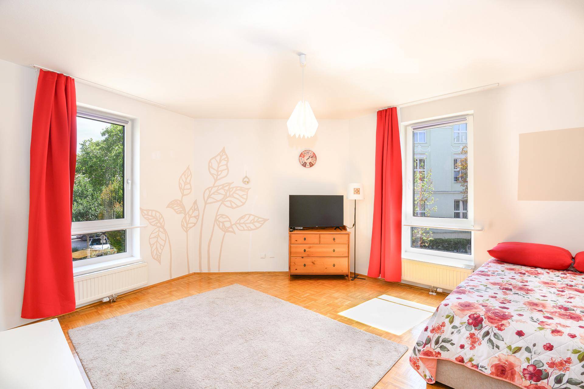 Helles Schlafzimmer mit Parkettboden, großen Fenstern und floraler Wanddekoration.