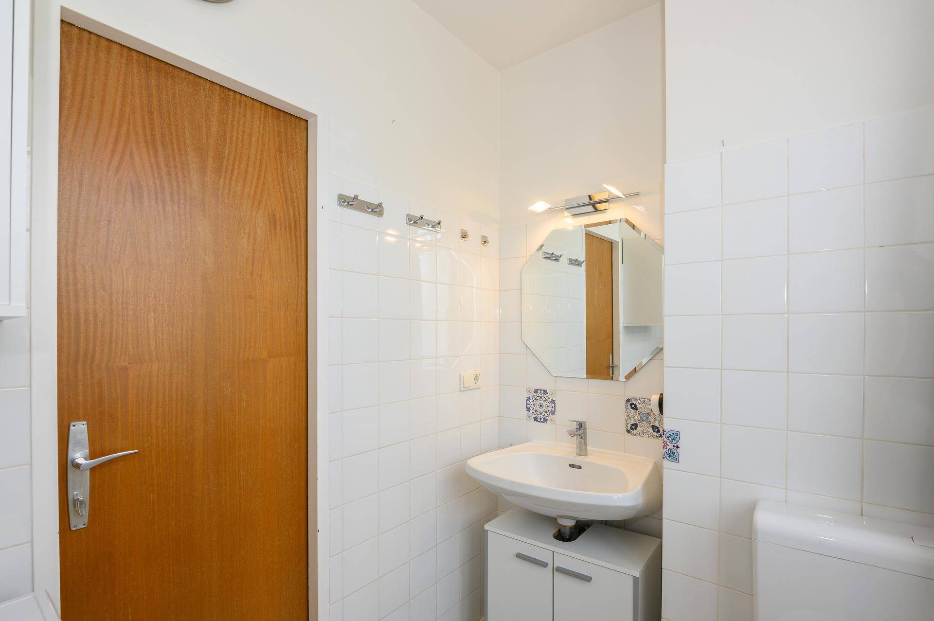 Badezimmer mit Waschbecken, Spiegel und weißen Fliesen.