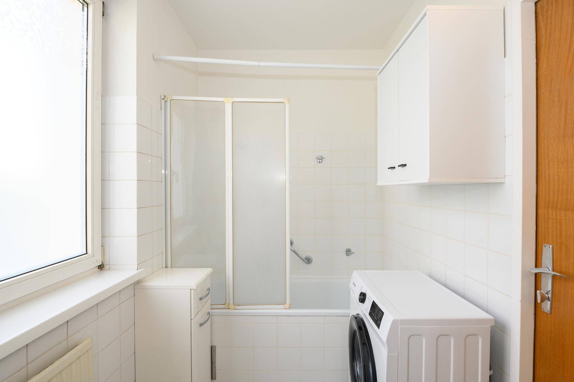Helles Badezimmer mit Badewanne, Duschabtrennung und Waschmaschine.