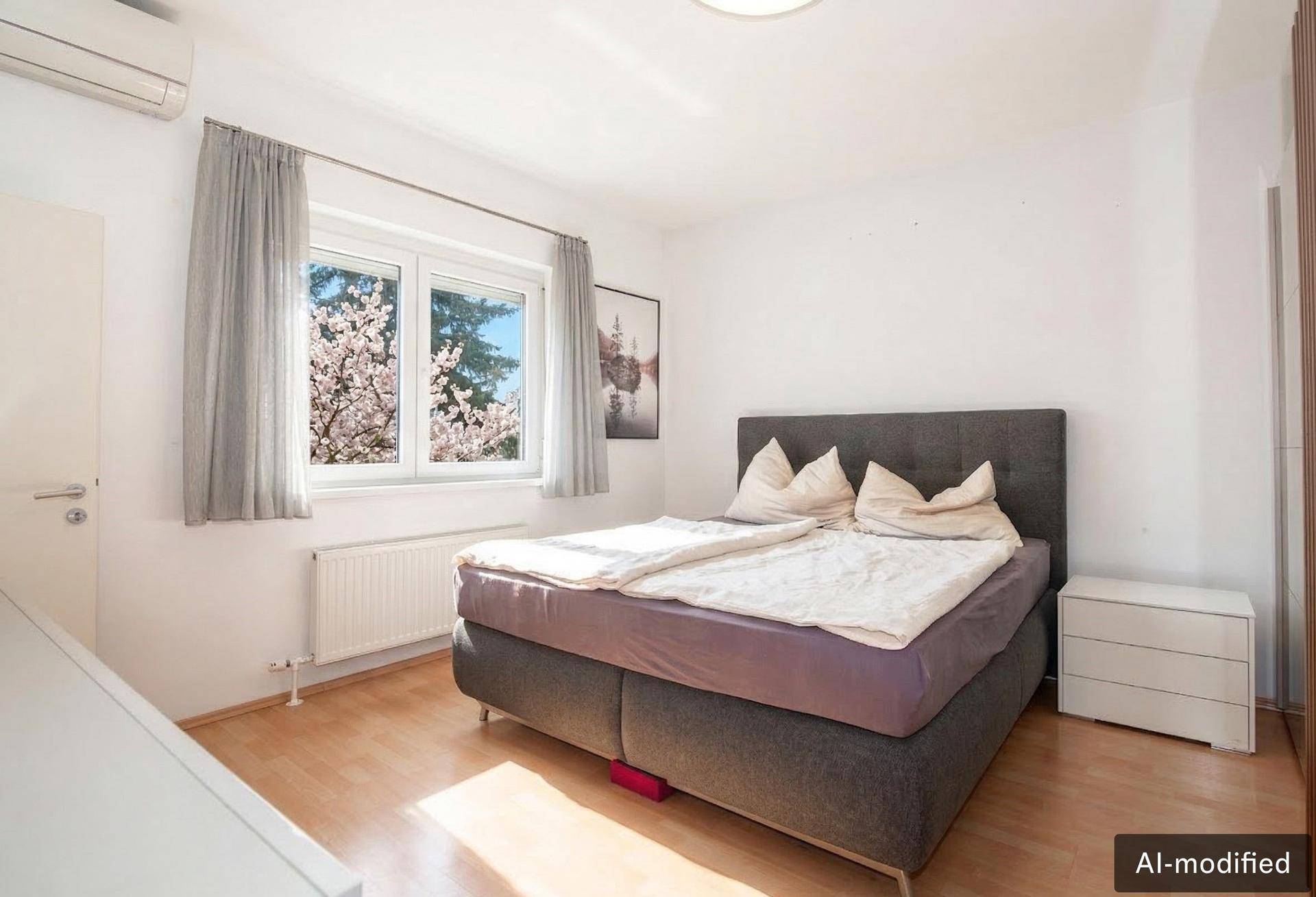 Helles Schlafzimmer mit Doppelbett, Holzboden, Klimaanlage und Fenster mit Blick ins Grüne.
