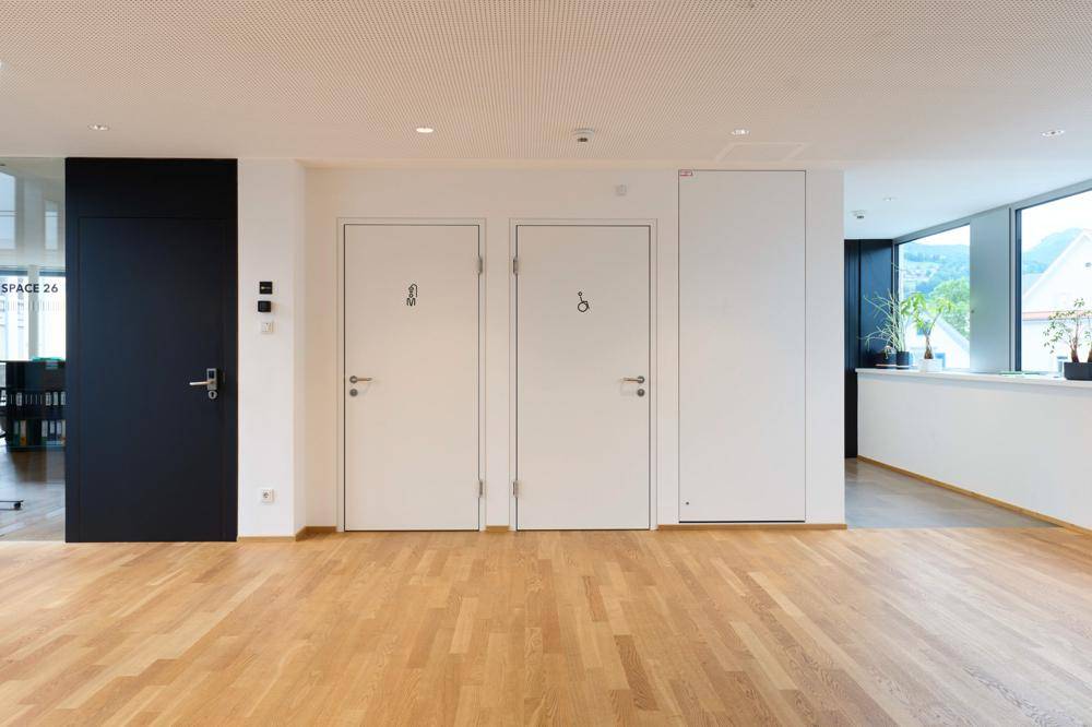 Heller Flur mit Holzboden und mehreren Türen, darunter barrierefreie Toiletten.