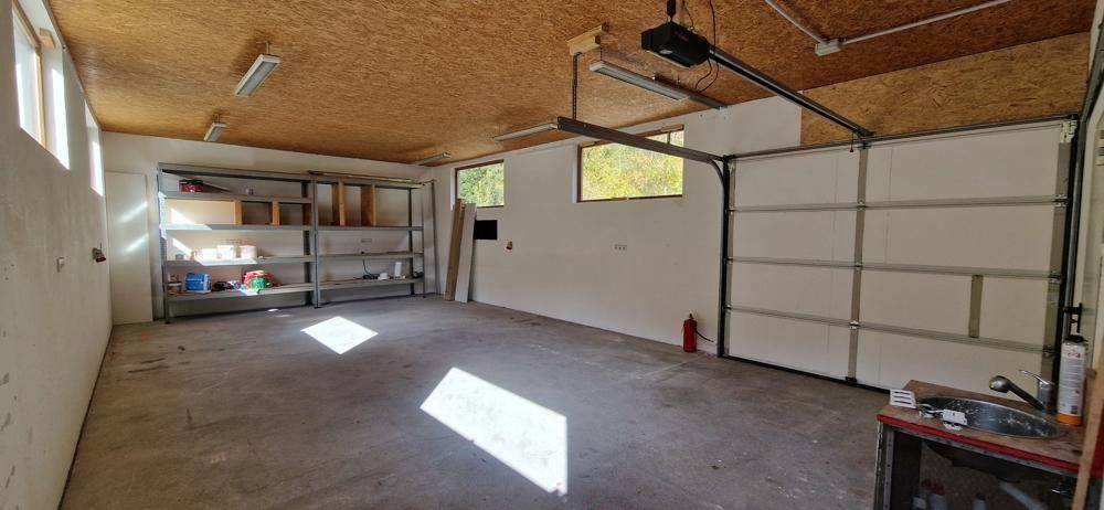 Geräumige Garage mit Betonboden, Regalen und einem Waschbecken, ideal für Lagerung oder Fahrzeuge.