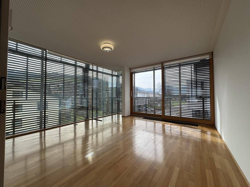 Geräumiger Raum mit Holzboden und einer großen Fensterfront, die viel Tageslicht hereinlässt.