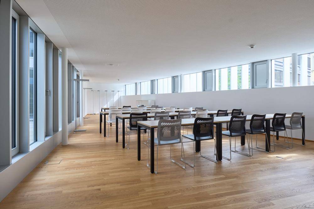 Weiterer Blick in den großen Konferenzraum mit Holzboden, Reihen von Tischen und Stühlen.