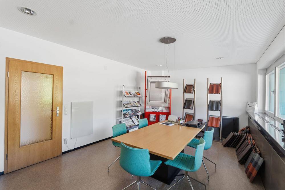 Besprechungsraum mit großem Holztisch, türkisfarbenen Stühlen und Produktmustern an der Wand.