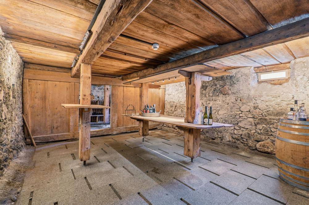Historischer Kellerraum mit Holzbalken, Steinwänden und einem Holztisch.