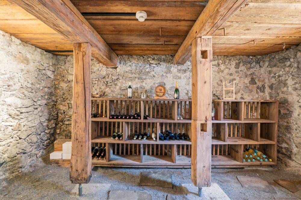 Weinkeller mit Holzregalen, Steinwänden und Holzbalken an der Decke.
