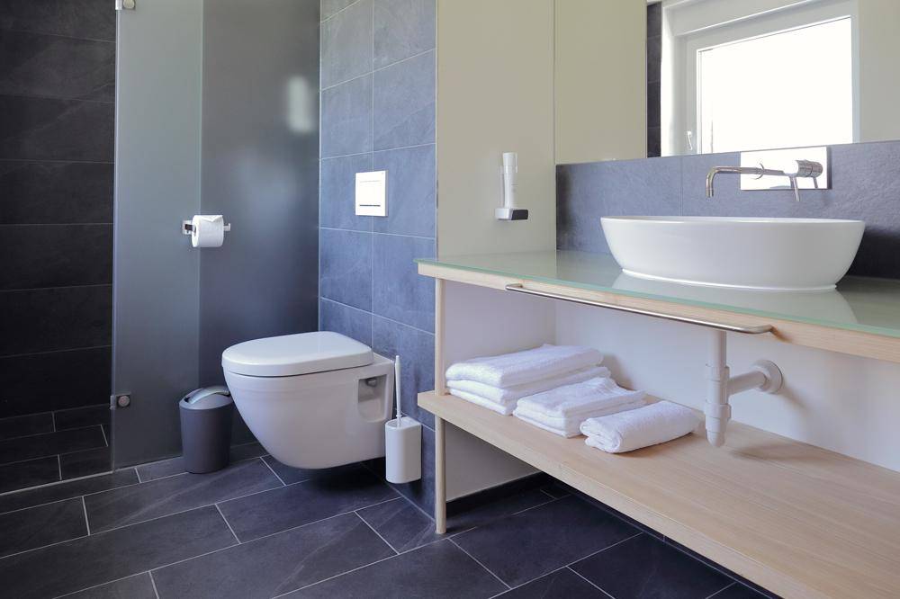 Modernes Badezimmer mit dunklen Fliesen, wandhängendem WC und begehbarer Dusche.