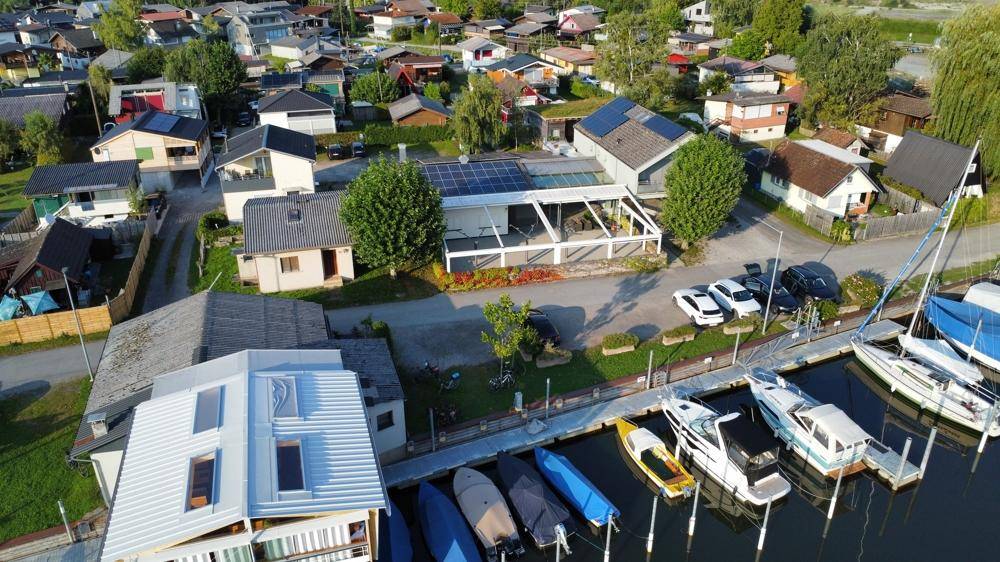 Weitläufige Luftaufnahme einer Siedlung am Wasser mit verschiedenen Gebäuden, Yachthafen und Bootsanlegestellen.