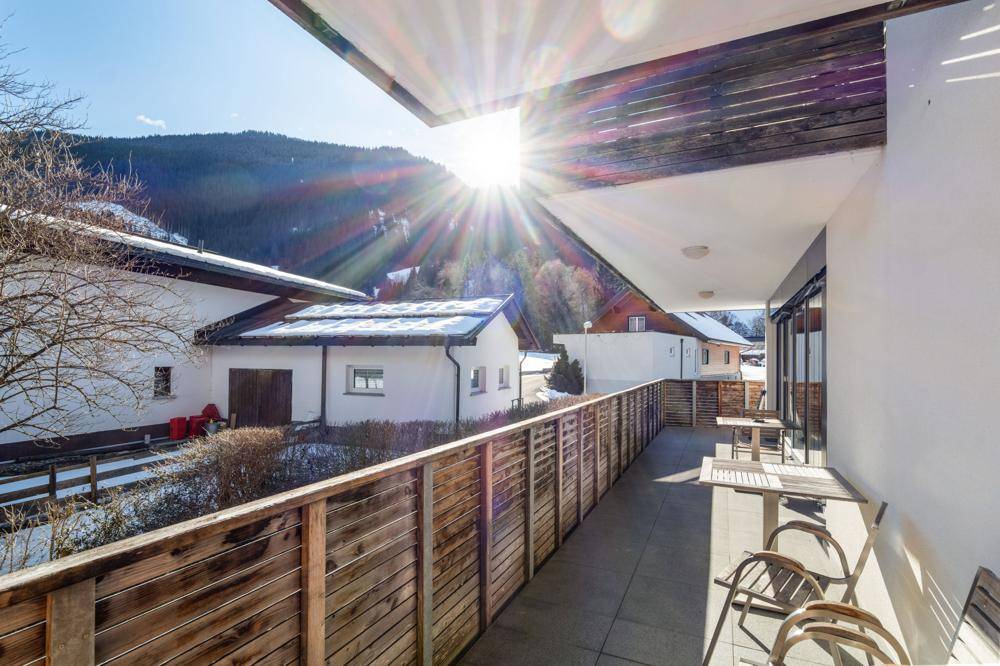 Sonniger Balkon mit Sitzgelegenheiten und Panoramablick auf die verschneite Landschaft.