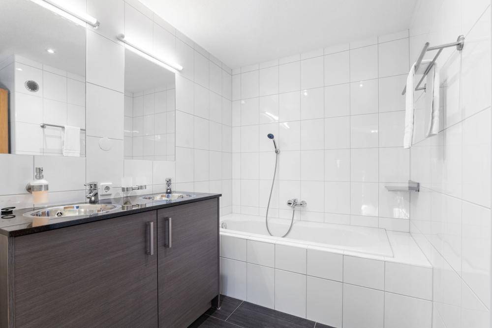 Modernes Badezimmer mit Doppelwaschbecken, Badewanne und weißen Fliesen.