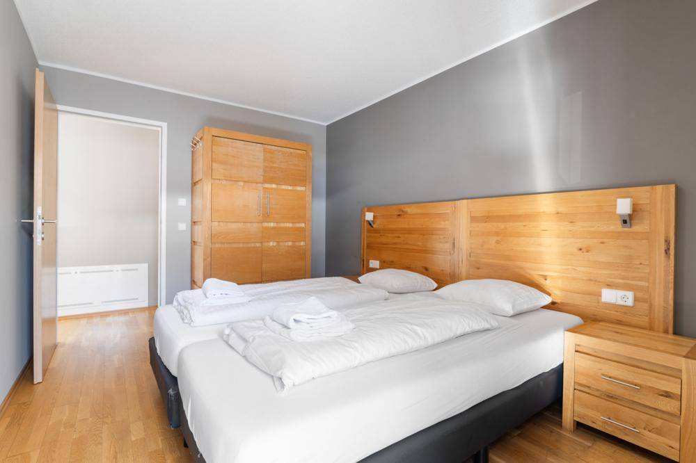 Schlafzimmer mit Holzbett, Kleiderschrank und Zugang zu einem weiteren Raum.