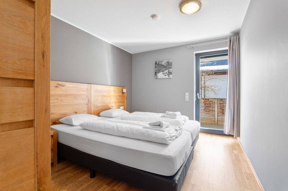Schlafzimmer mit Holzbett und Zugang zu einem Balkon, der viel Licht hereinlässt.