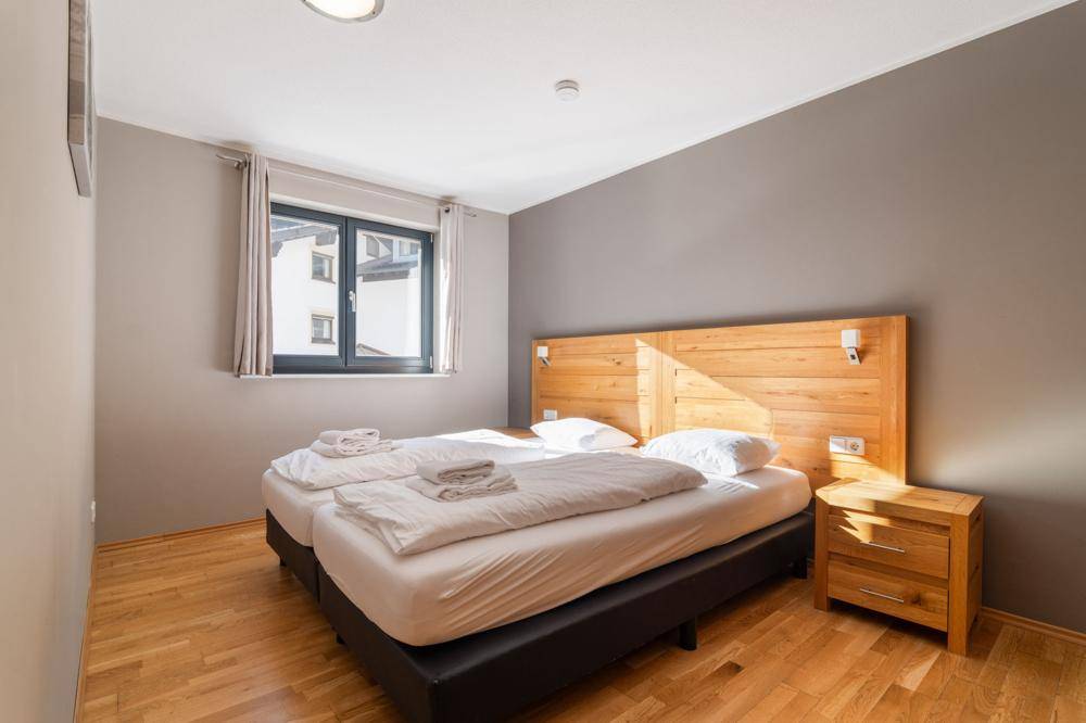 Helles Schlafzimmer mit Holzbett, Nachttisch und Fenster mit Blick nach draußen.