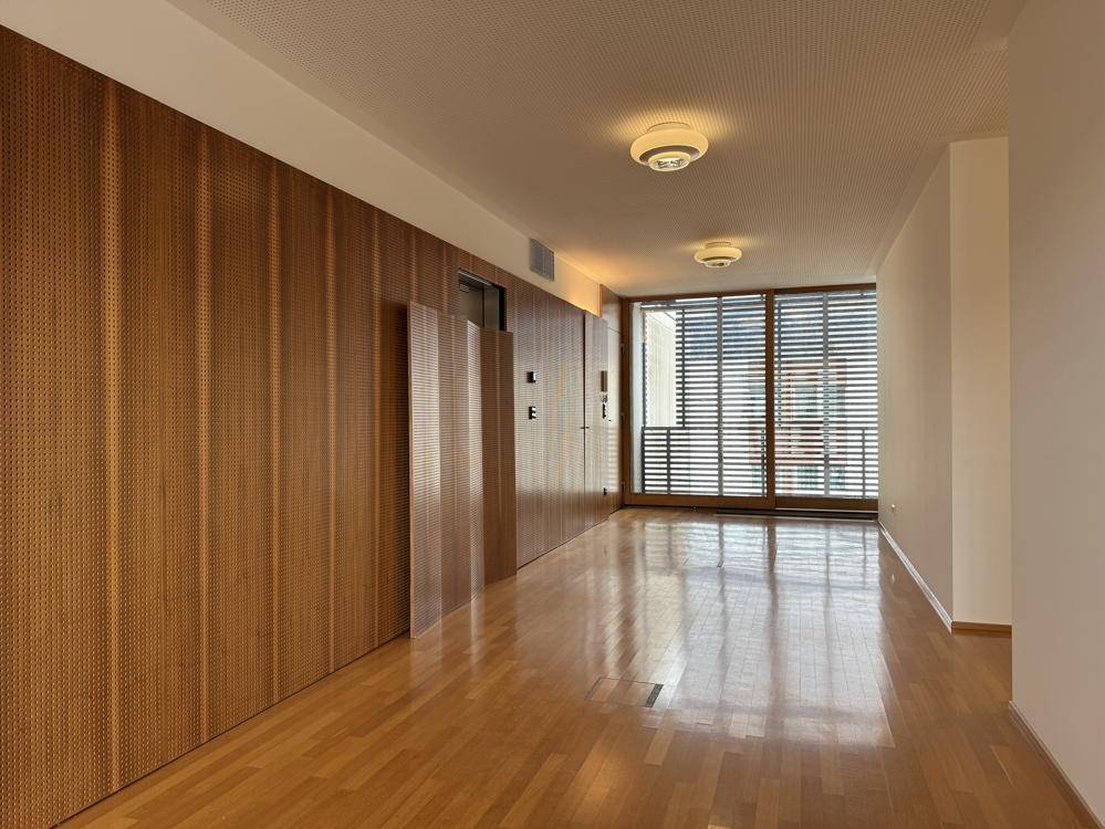 Langer Flur mit Holzboden und einer eleganten Wandverkleidung aus Holz, die zu einem Fensterbereich führt.