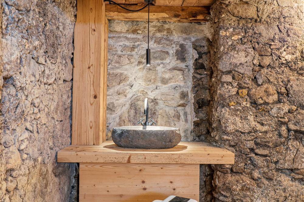 Rustikales Badezimmer mit Steinwaschbecken, Holzablage und Natursteinwänden.