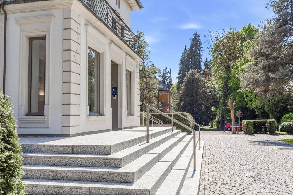 Elegante Steintreppe führt zum Eingang des Gebäudes, ergänzt durch eine barrierefreie Rampe mit Handlauf.