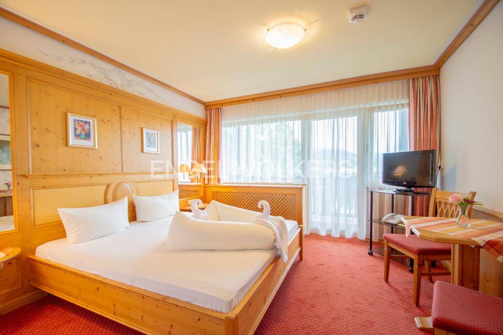 Geräumiges Schlafzimmer mit Doppelbett, Teppichboden, TV und Zugang zu einem Balkon.