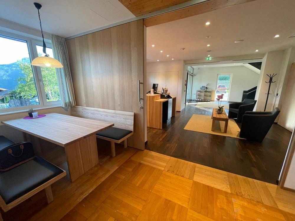 Empfangsbereich mit Holzboden und Sitzgelegenheiten, angrenzend an einen Essbereich mit Bank.