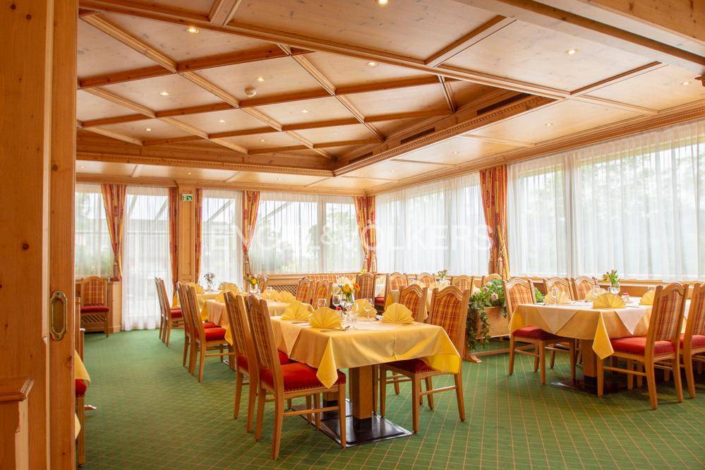Großer Speisesaal mit vielen Tischen, Teppichboden und großen Fenstern für viel Tageslicht.