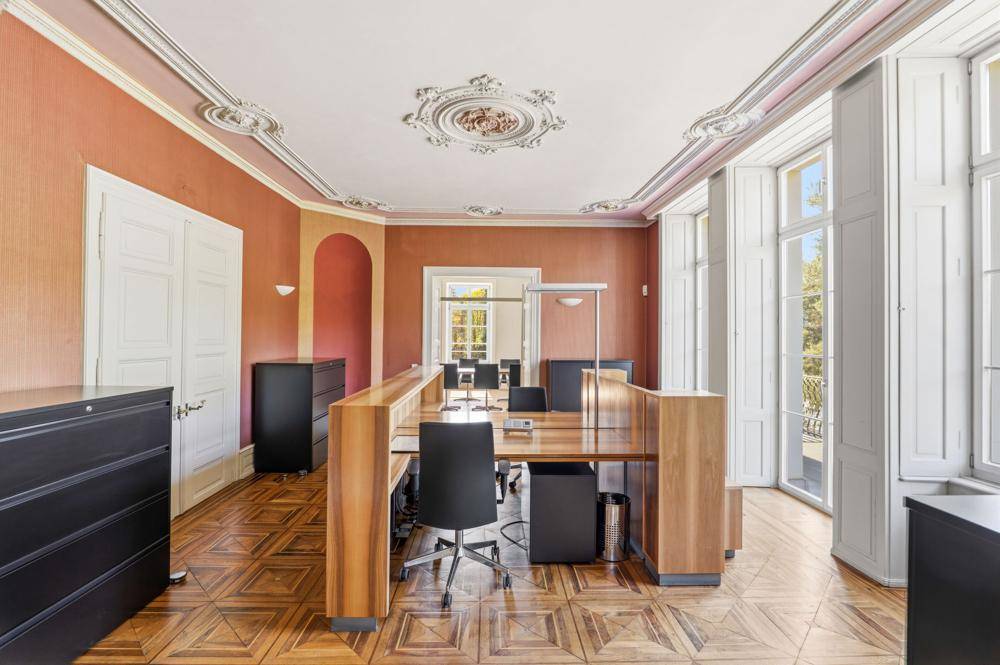 Großzügiges Büro mit Holzböden, hohen Fenstern und klassischer Stuckverzierung an der Decke, gut beleuchtet.