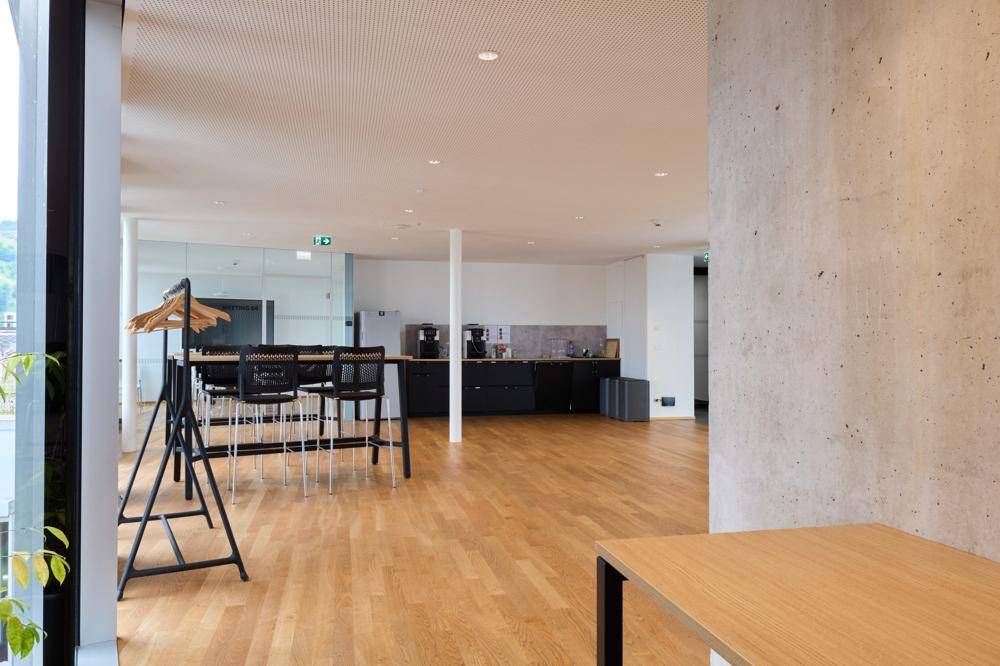 Moderner, offener Bürobereich mit Kaffeestation, hohen Tischen und Blick nach draußen, perfekt für informelle Besprechungen.