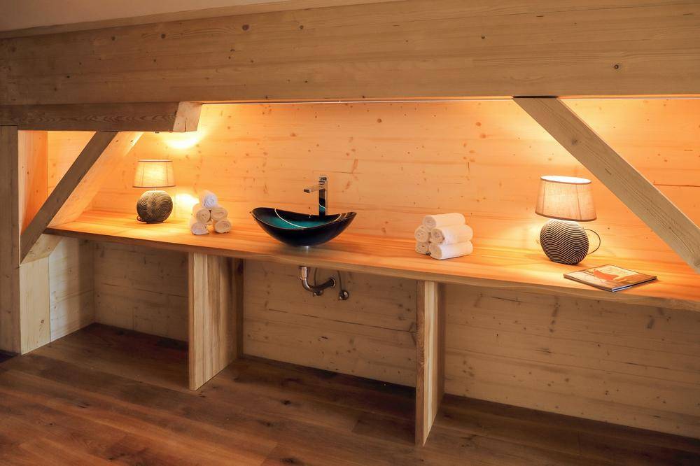 Waschtischbereich mit Holzplatte, modernem Waschbecken und indirekter Beleuchtung unter Dachschräge.