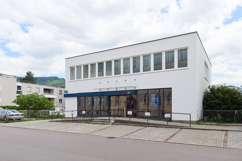 Modernes weißes Geschäftsgebäude mit großen Schaufenstern und Parkplätzen im Freien.