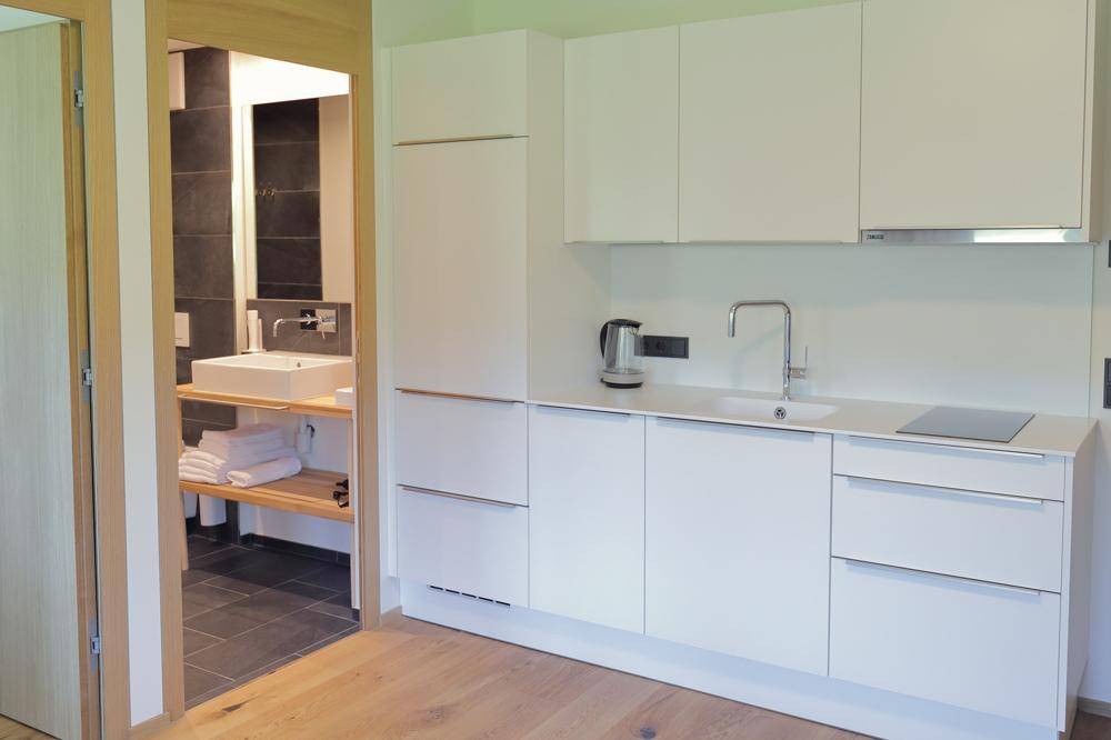 Moderne, weiße Küchenzeile mit Induktionskochfeld und Spüle, angrenzend an ein Badezimmer.
