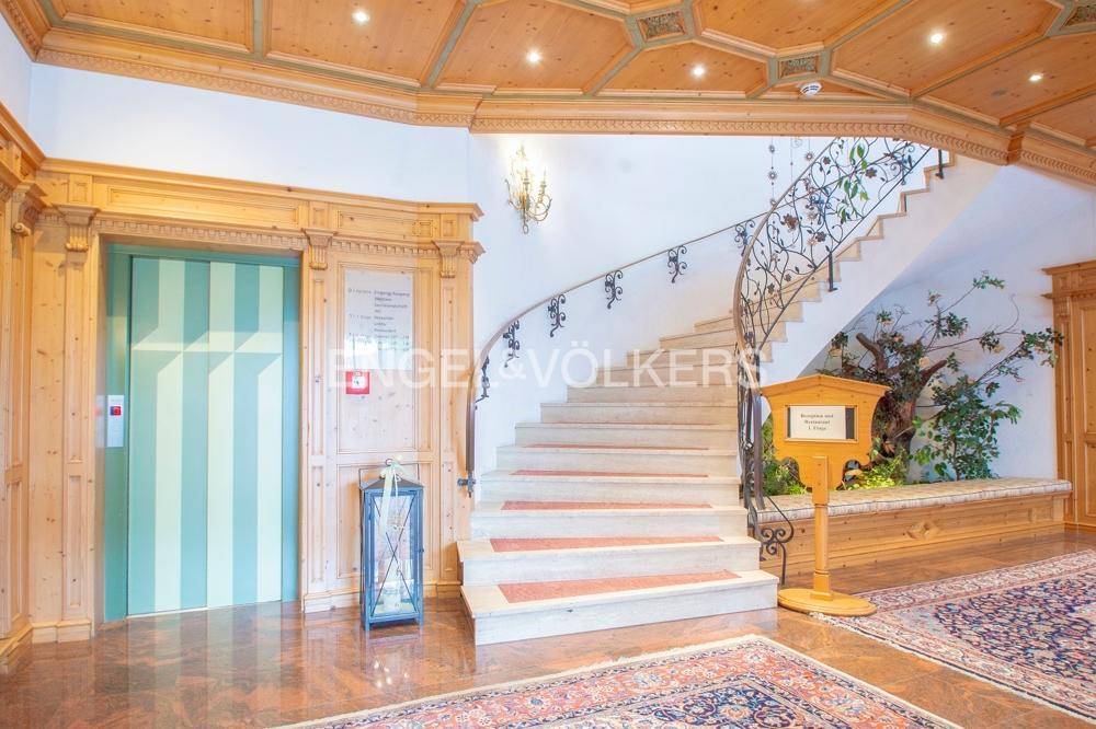 Elegante Hotellobby mit einer geschwungenen Marmortreppe, Aufzug und Holzelementen.