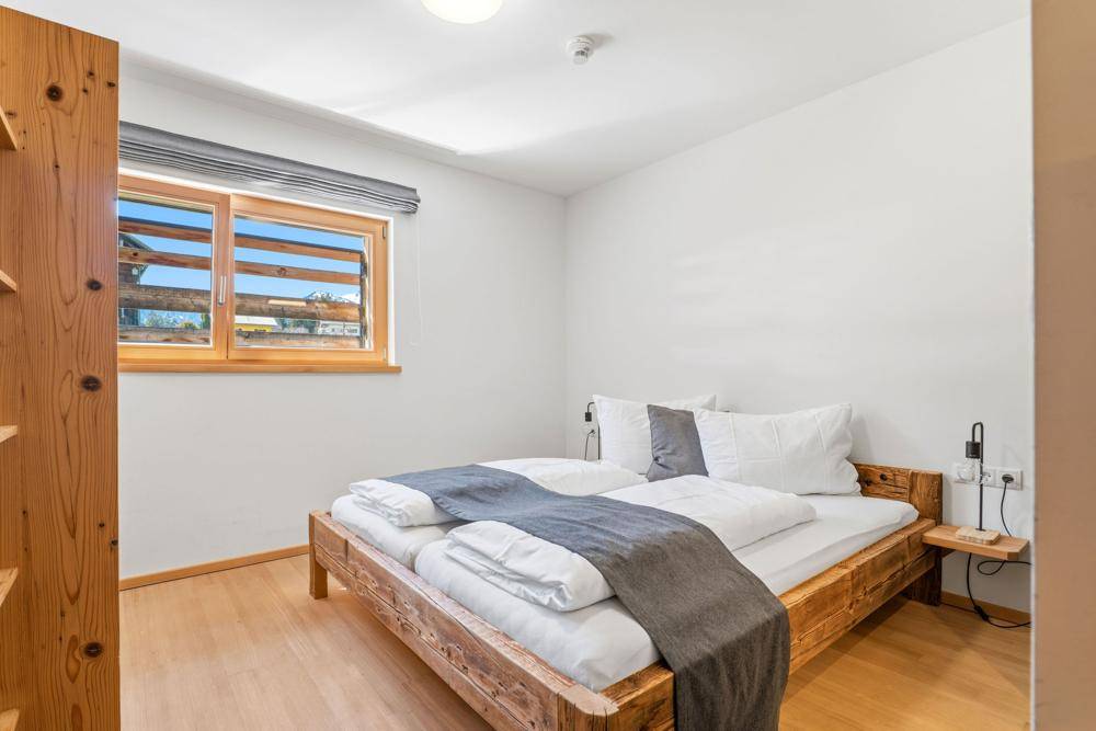 Gemütliches Schlafzimmer mit Holzbett, Holzboden und einem Fenster mit Blick auf die grüne Landschaft.