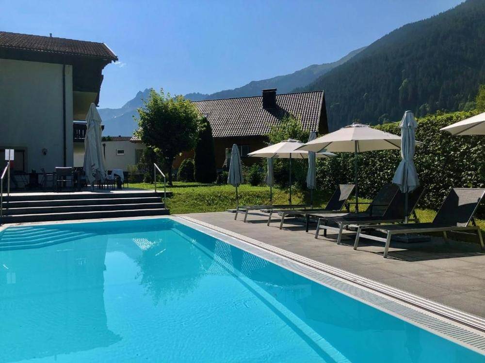 Sonniger Poolbereich mit Liegemöglichkeiten und weitem Blick auf die umliegende Berglandschaft.