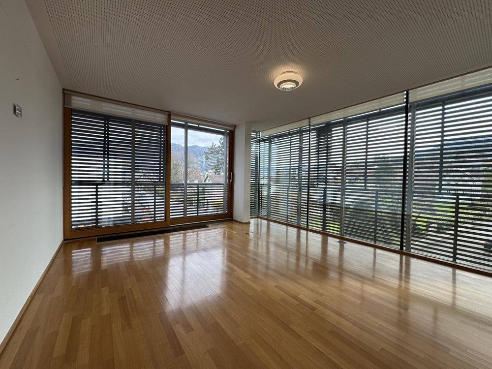 Heller Raum mit Holzboden und einer breiten Fensterfront, die viel natürliches Licht spendet.