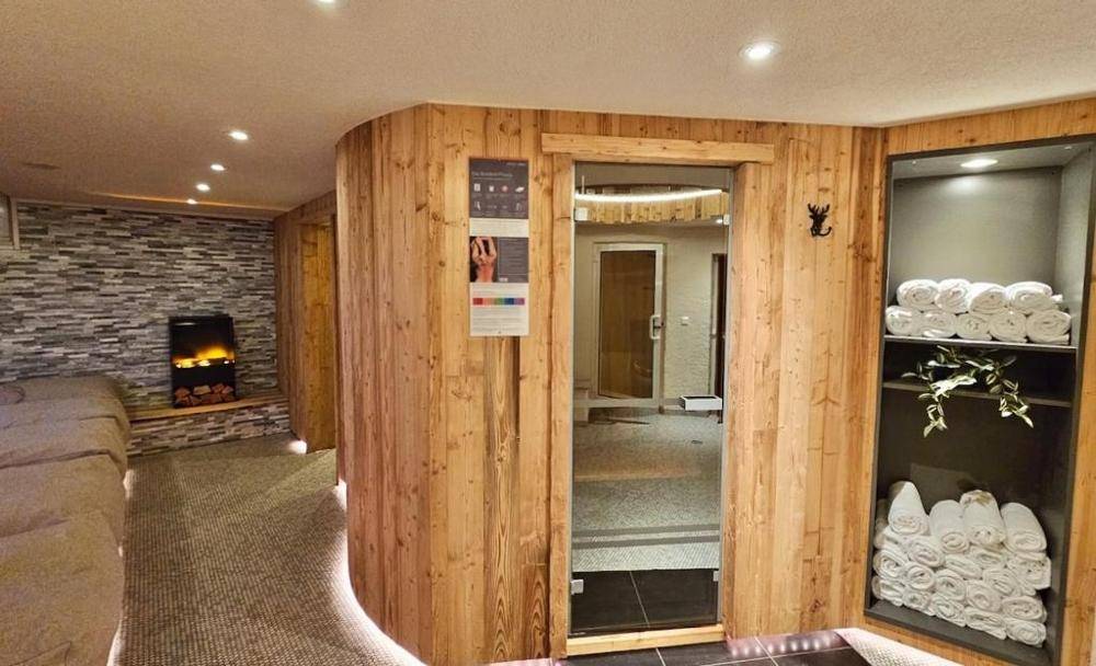 Gemütlicher Wellnessbereich mit Sauna, Entspannungsliege und dekorativem Kamin in Holzoptik.
