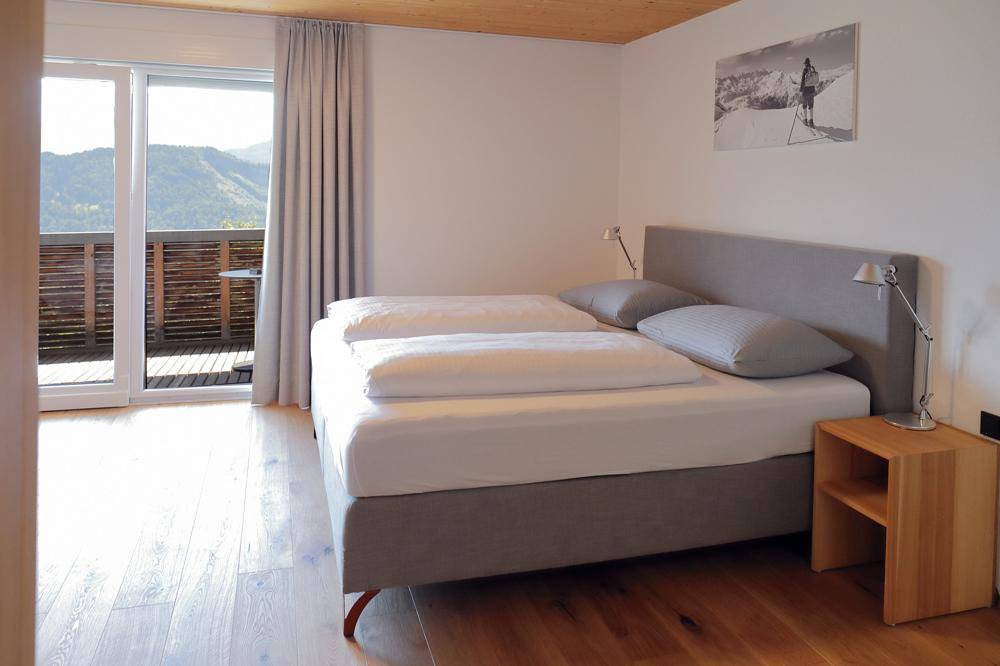 Helles Schlafzimmer mit Doppelbett, Holzboden und Zugang zu einem Balkon mit Bergblick.