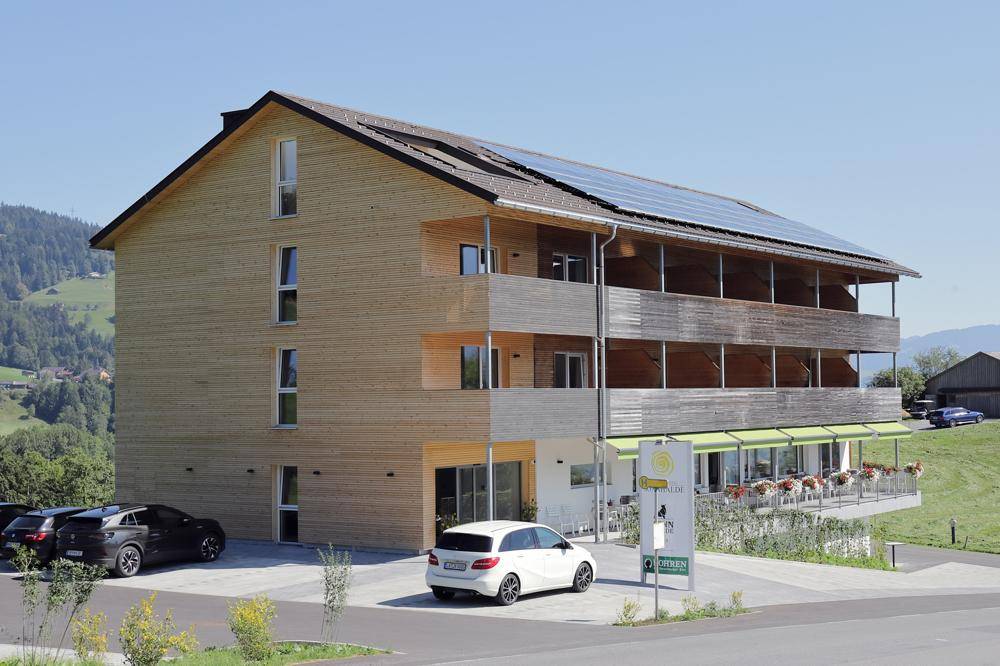Neues Holzhotel mit Balkonen, Solarpaneelen auf dem Dach und Parkplätzen im Grünen.