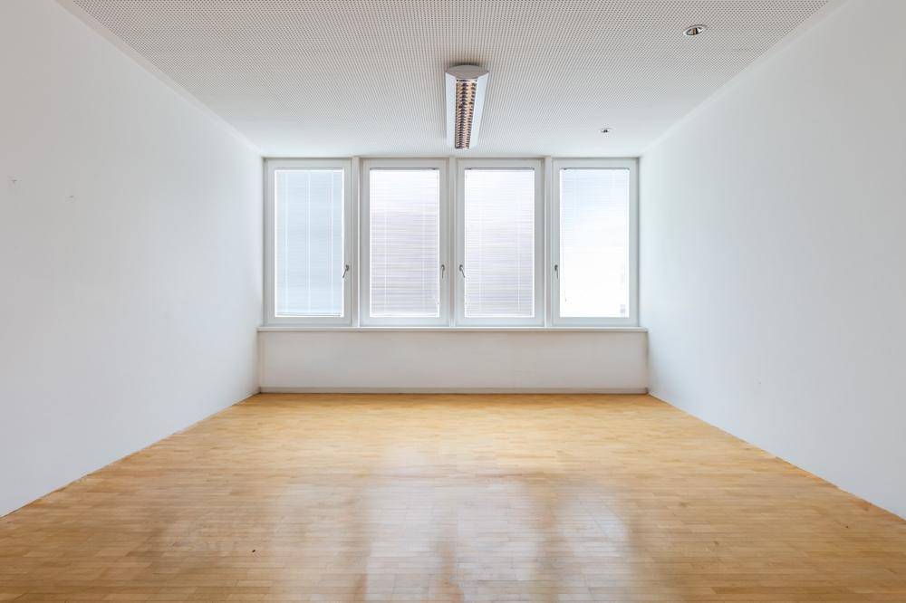 Langer, heller Büroraum mit Parkettboden, großen Fenstern und einer zentralen Deckenleuchte.