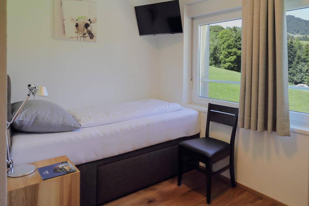 Gemütliches Einzelzimmer mit Holzboden, Fenster und Blick auf die grüne Landschaft.