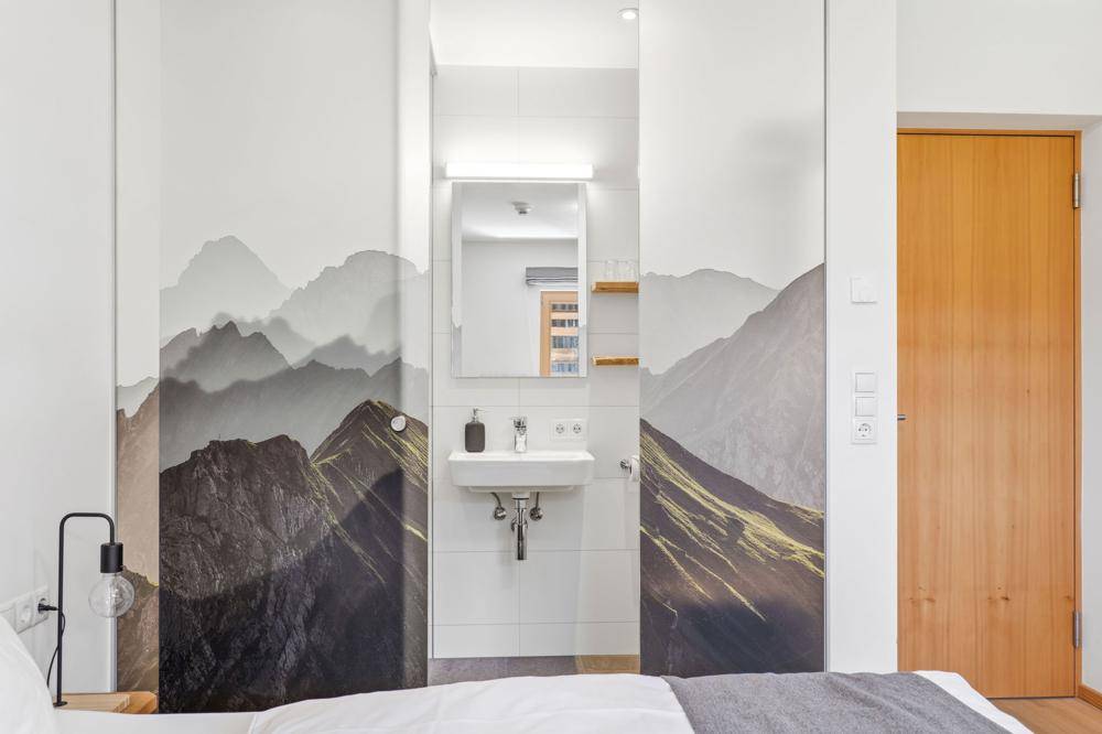 Schlafzimmer mit integriertem Waschbeckenbereich, modernen Wandbildern und Holztür.