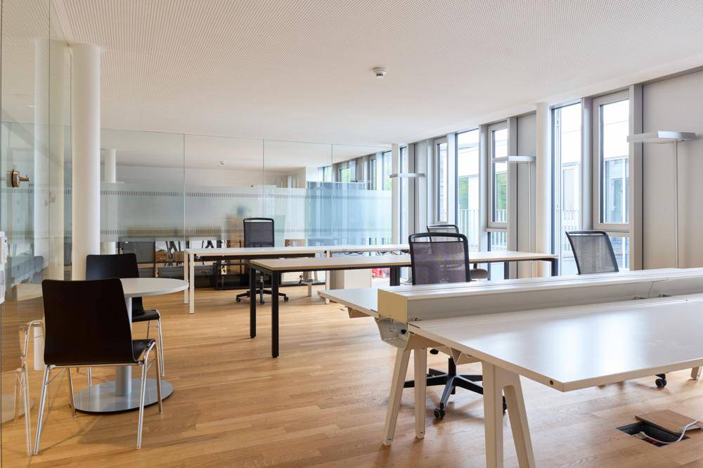 Offener Bürobereich mit Glaswänden, Holzboden und modernen Arbeitsplätzen mit Blick nach draußen.
