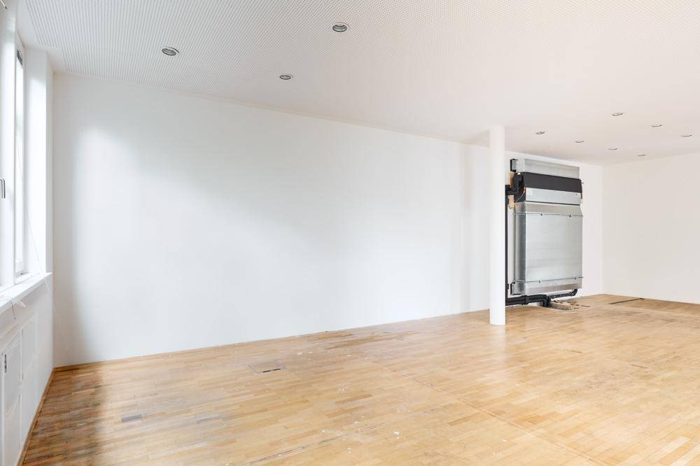 Großer, leerer Büroraum mit Parkettboden, weißen Wänden und einem Lüftungssystem.