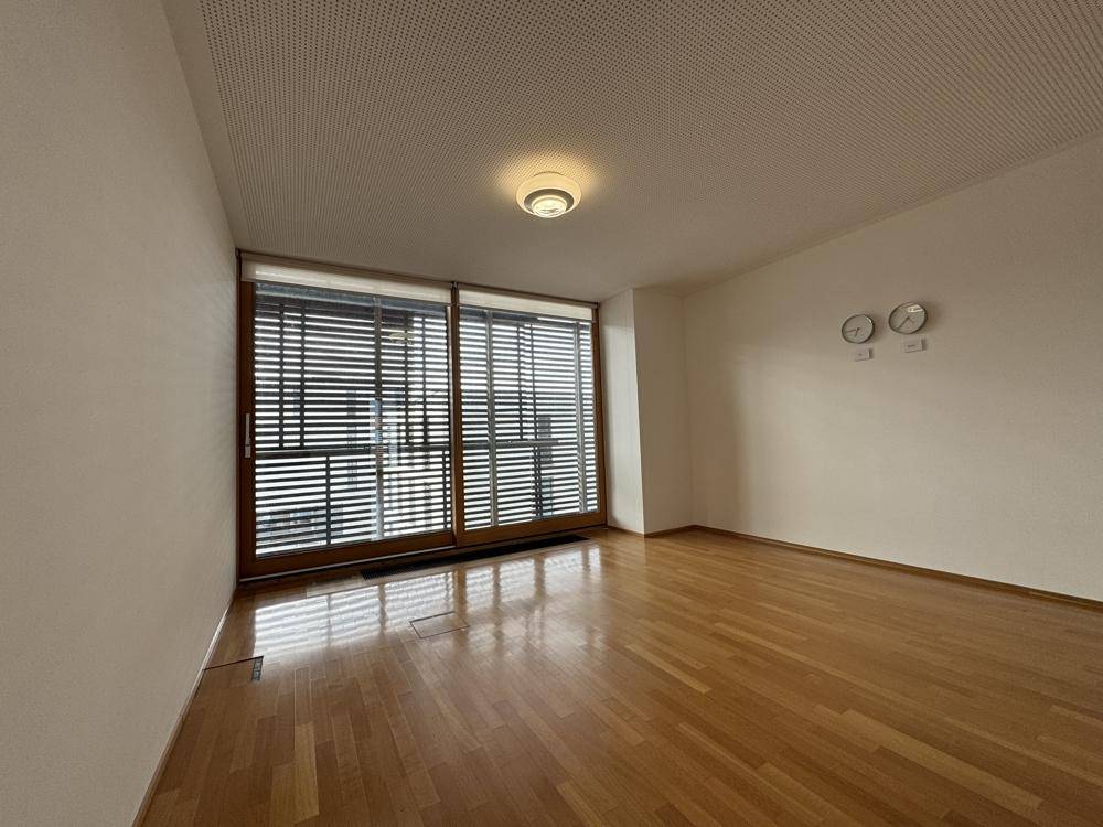 Geräumiger Raum mit Holzboden und einer breiten Fensterfront, die viel Licht spendet.