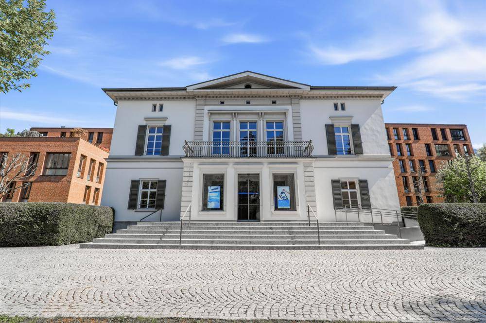 Klassisches Gebäude mit eleganter weißer Fassade, großen Fenstern und einem Balkon über dem Haupteingang.