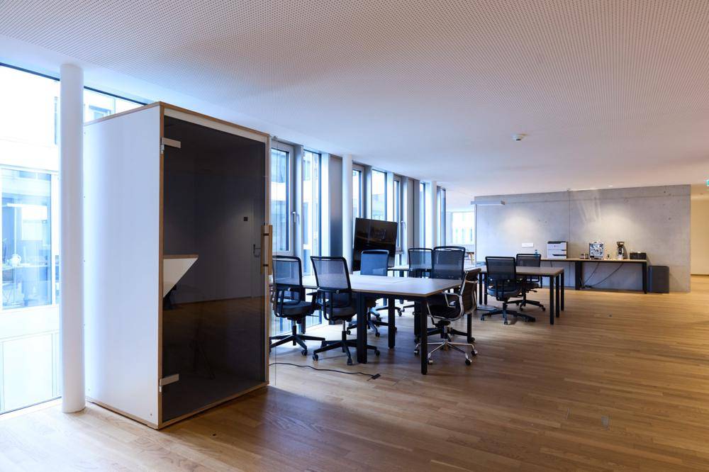 Offener Bürobereich mit Holzboden, Arbeitsplätzen und einer schallgedämmten Telefonkabine.