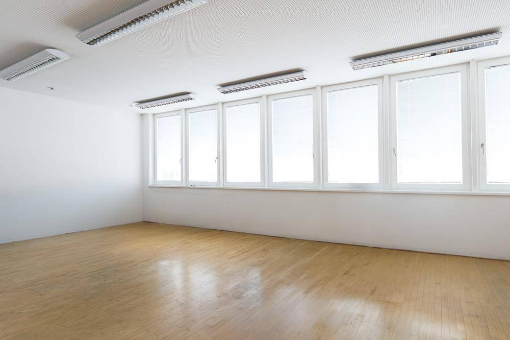 Heller Büroraum mit Parkettboden, einer langen Fensterfront und mehreren Leuchtstoffröhren.