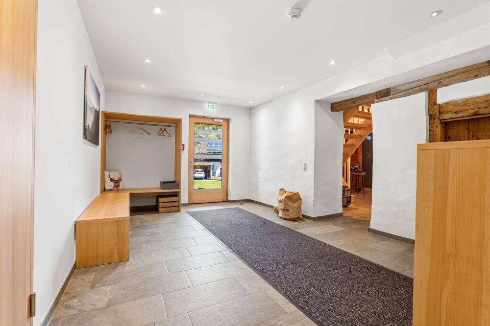 Heller Eingangsbereich mit Fliesenboden, Garderobe und Blick nach draußen durch die Glastür.