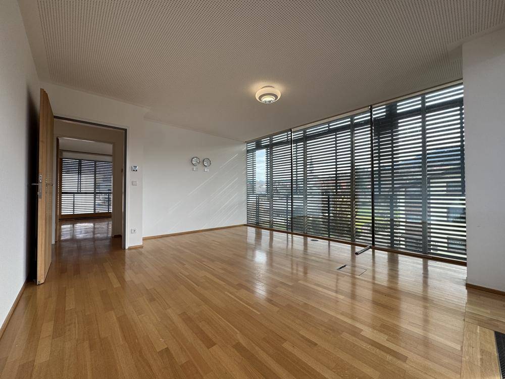 Heller Raum mit Holzboden und einer Fensterfront, die viel natürliches Licht hereinlässt.