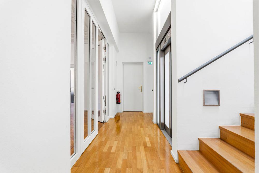 Heller Flur mit Holztreppe, Aufzug und glänzenden Parkettböden, bietet Zugang zu den Büros.